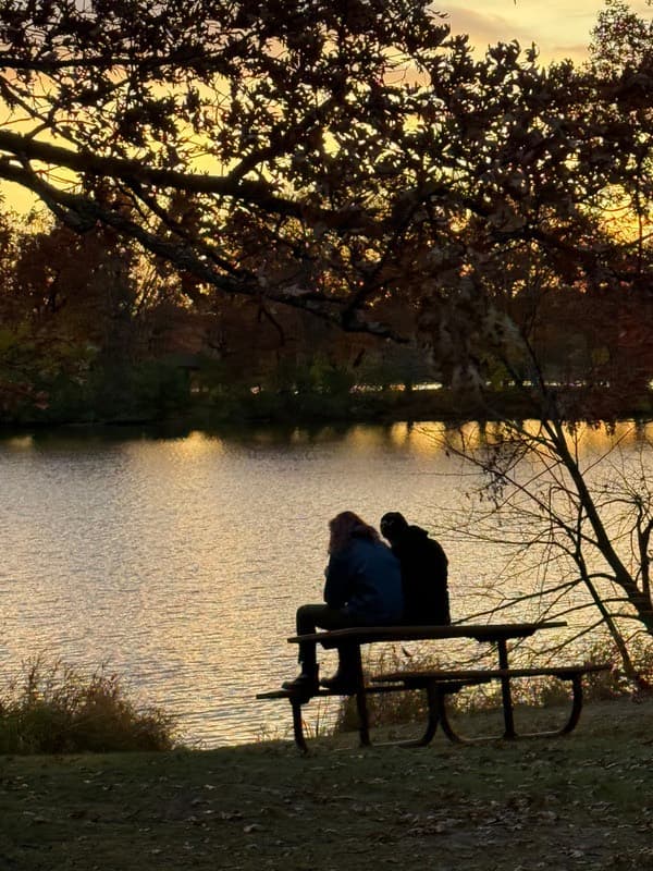Two people sitting on a picnic table watching the sun set over Silver Lake in autumn