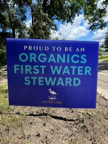 An “Organics First Water Steward” yard sign in a lakeside yard